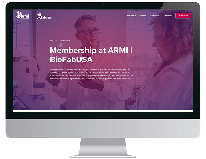 A computer screen displays the ARMI BioFabUSA membership webpage with two people in lab coats talking.