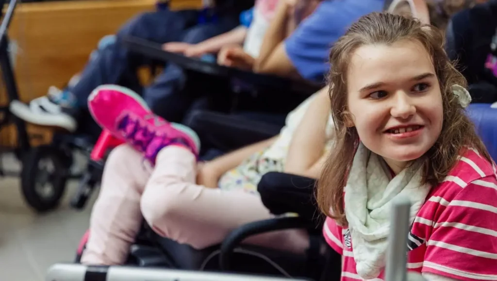 Smiling girl in a striped shirt and scarf sits indoors with others, including someone in a wheelchair, as they discuss a rebranding case study.