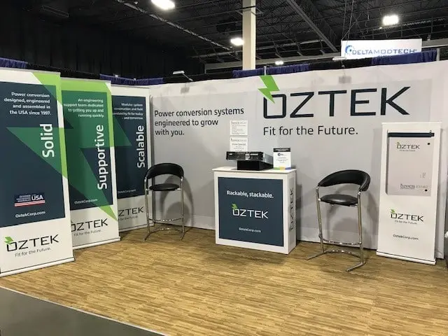 Oztek trade show booth with banners, two chairs, a table, and promotional materials on display, showcasing their expertise in manufacturing website design.