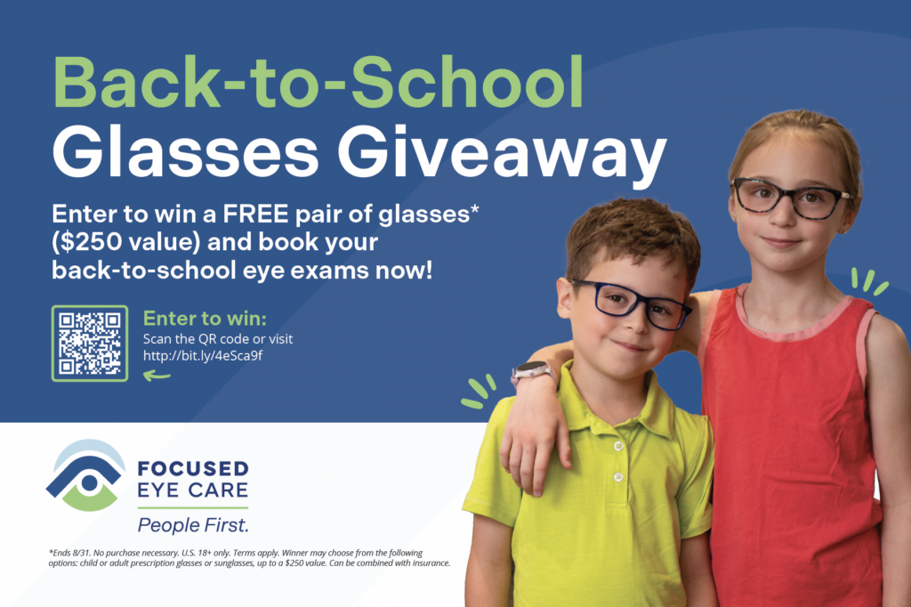 Two children with glasses smile in front of a Back-to-School Glasses Giveaway sign for Focused Eye Care.