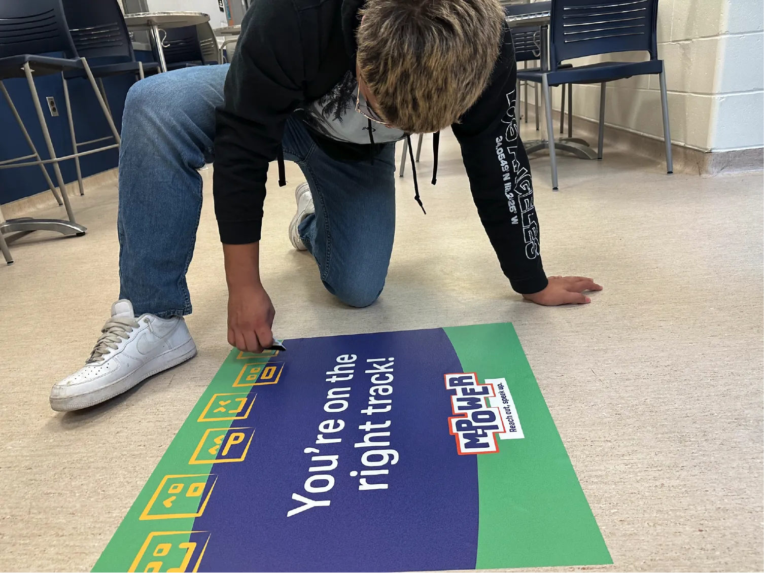 Person kneeling on floor, placing a sign that says, You&rsquo;re on the right track! with a Mower County logo.