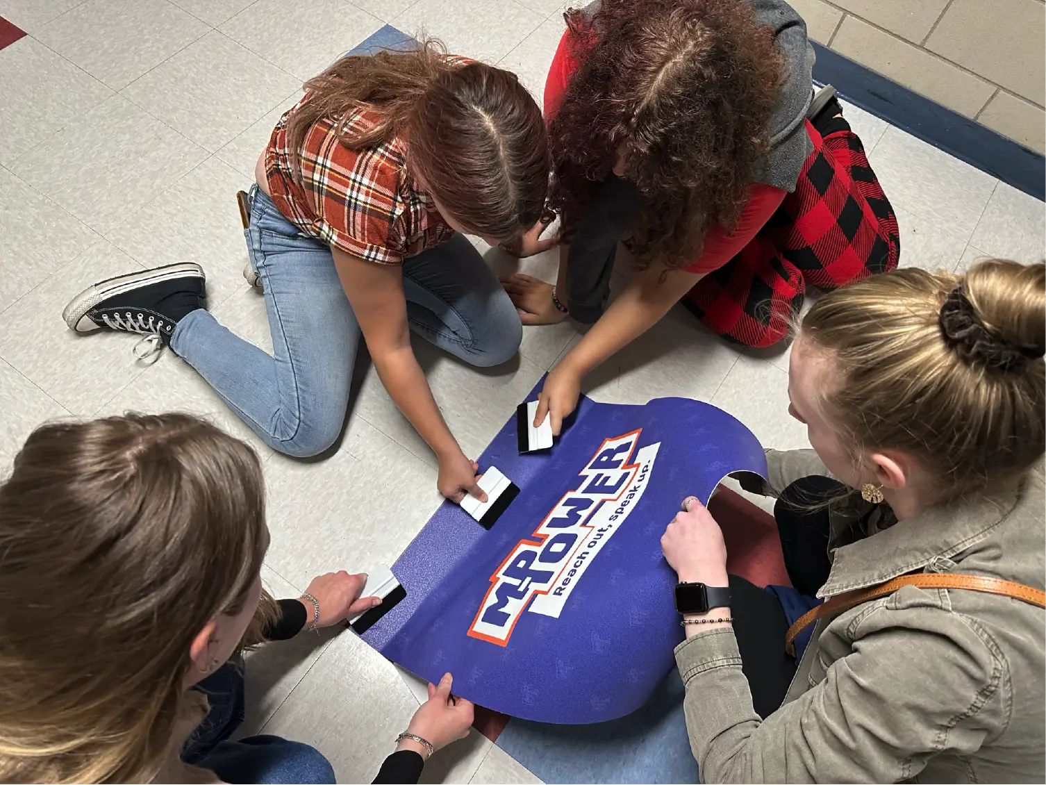 Four people kneel on the floor, inserting cards into a box labeled My POWER: Pride, Ownership, Wisdom&mdash;a powerful scene of community and collective spirit.