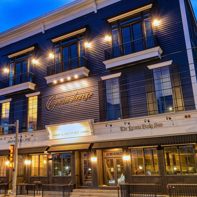 A lit-up three-story building with balconies and large windows at dusk, featuring restaurants, offices, and modern marketing spaces.