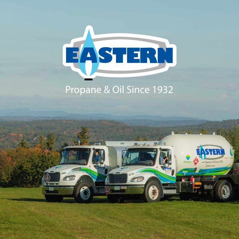 Two Eastern propane trucks on a grassy field with forest and mountains in the background; company logo above, highlighting the company's strong marketing presence.