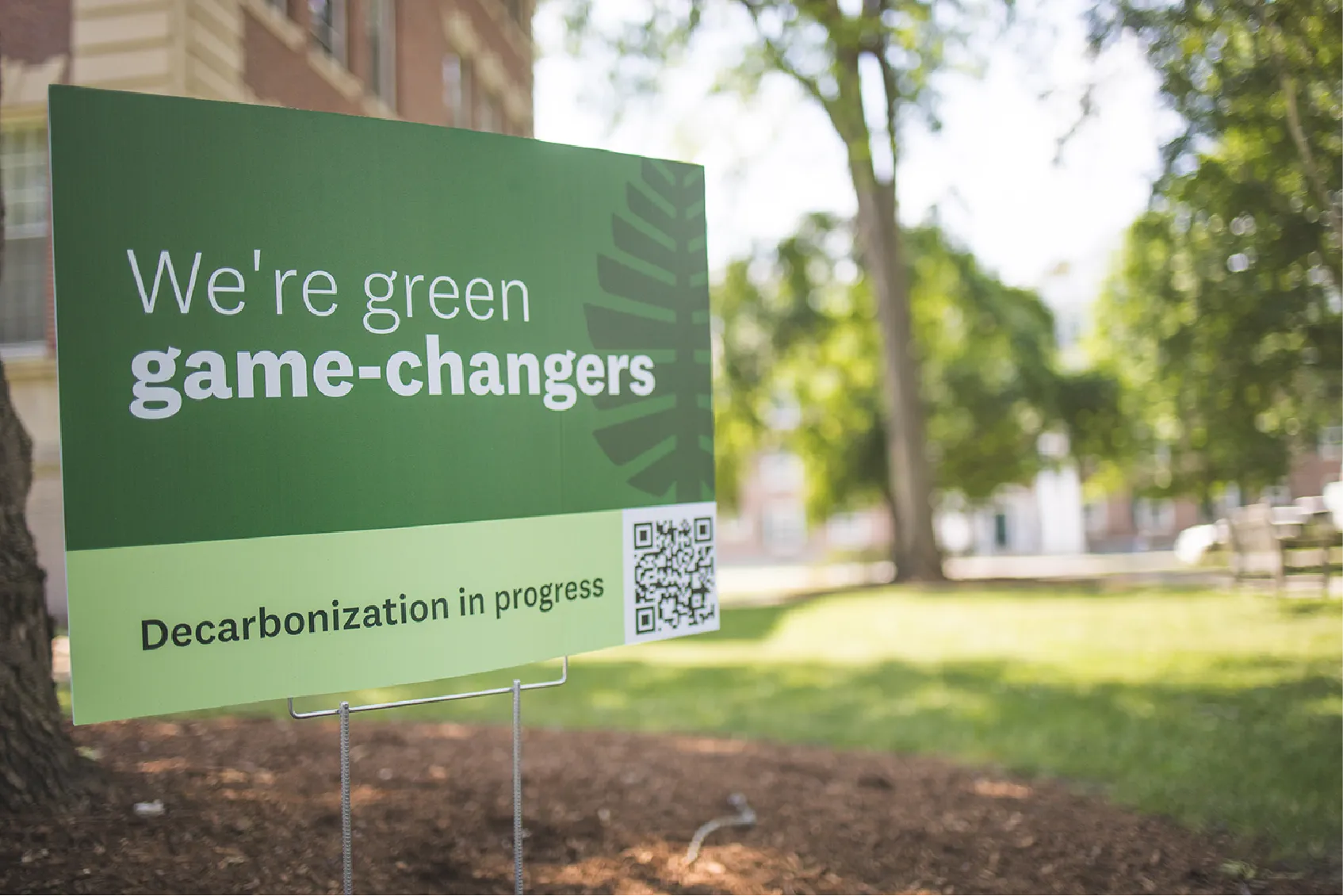 A green sign on a lawn reads, Were green game-changers. Decarbonization in progress.