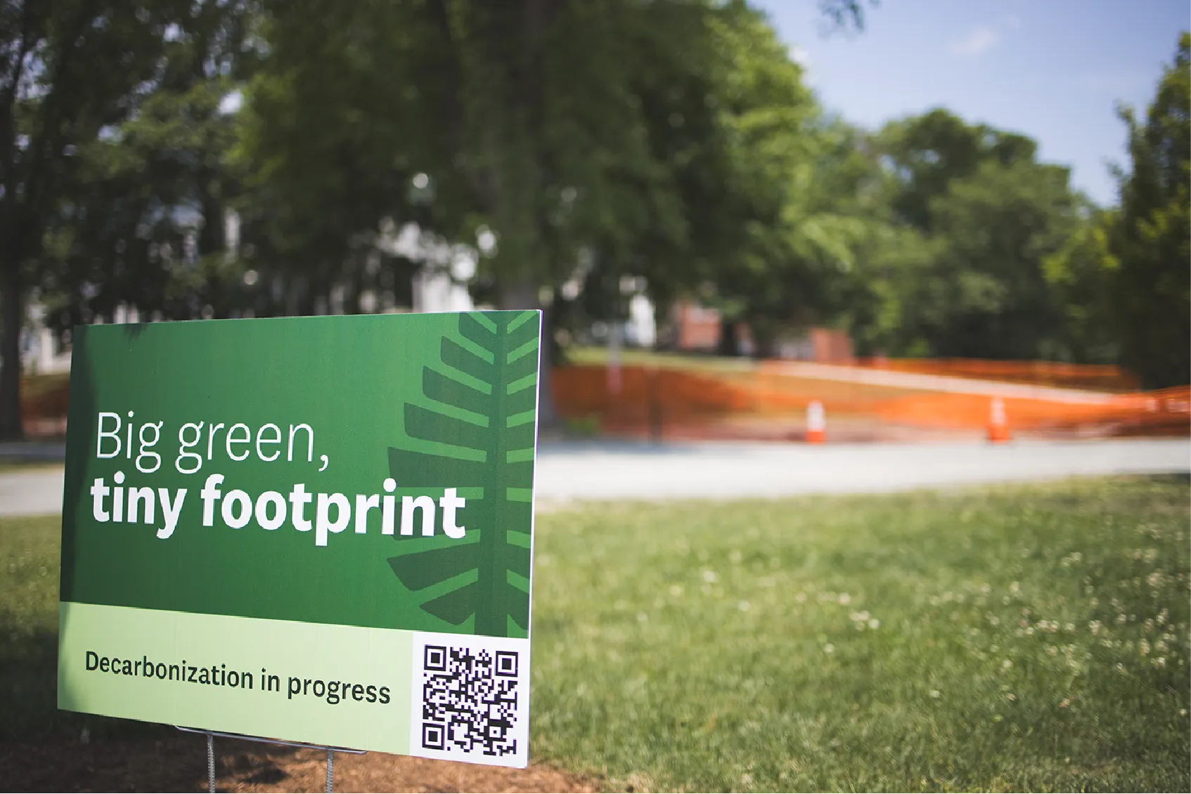 Green sign on grass reads Big green, tiny footprint. Decarbonization in progress with a QR code.