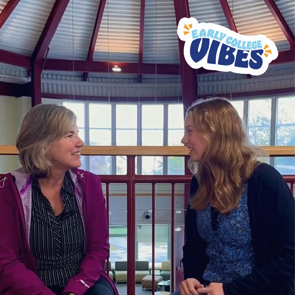 Two women sit indoors talking and smiling under a skylight, sharing early college vibes and growth marketing ideas. Text reads &ldquo;Early College Vibes&rdquo; in the corner.