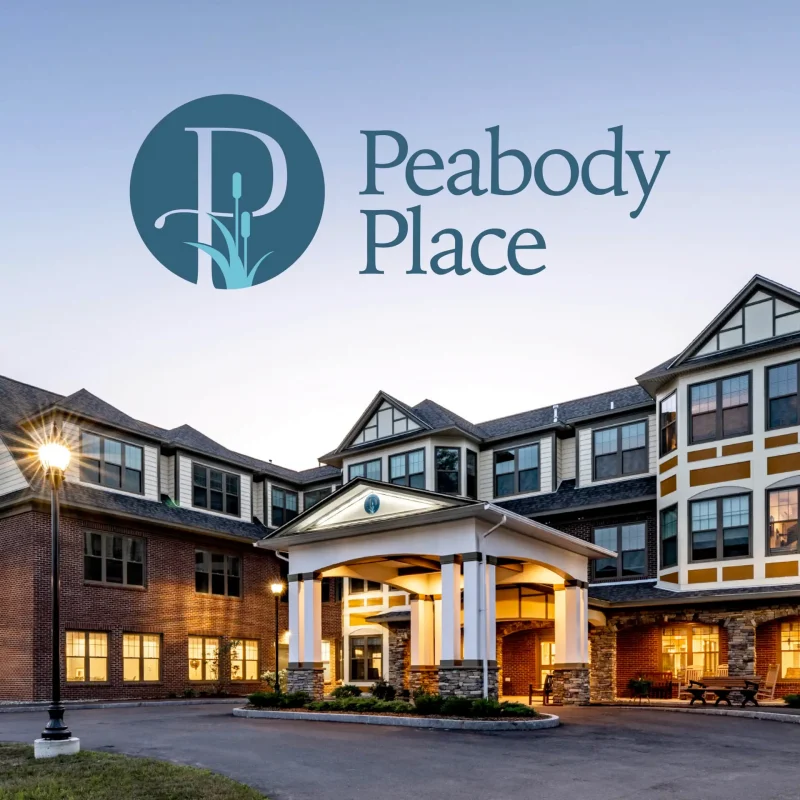 Exterior view of Peabody Place, a large, well-lit senior living facility at dusk with logo above&mdash;a welcoming sight featured in the community's marketing materials.